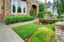 A home's front yard with trimmed shrubs, flowers, and low stone walls.