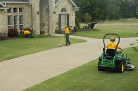 Two Grounds Guys service professionals mowing and edging a home's front lawn.