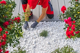 The Grounds Guys service professional installing white pebbles in a garden bed.