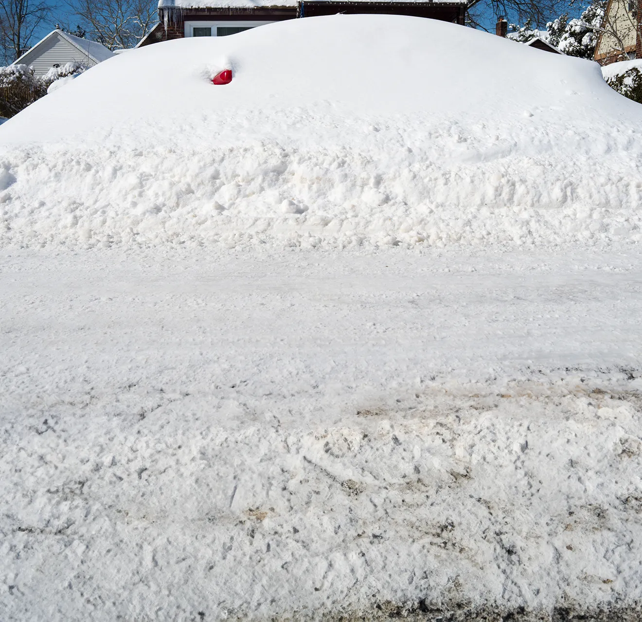 A car on a residential street buried in snow after a blizzard.