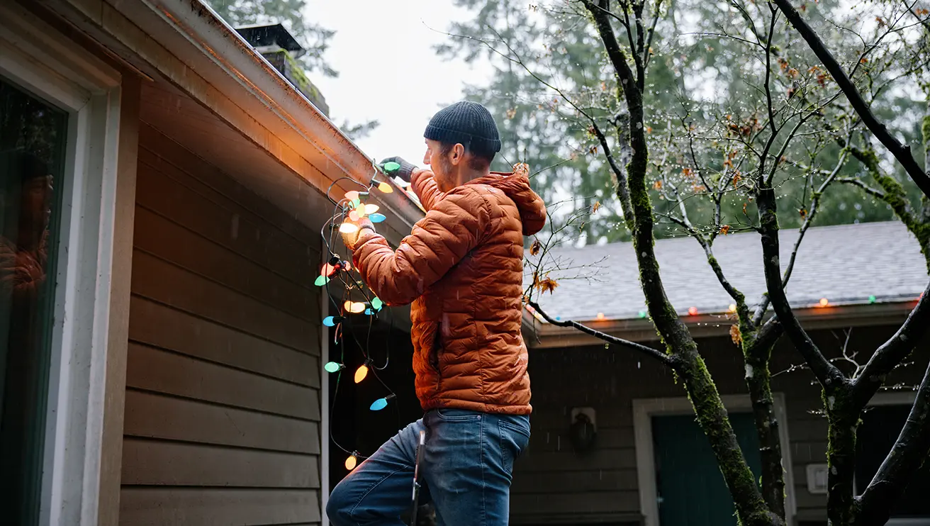 Middle aged Caucasian man hanging Christmas holiday lighting on house.