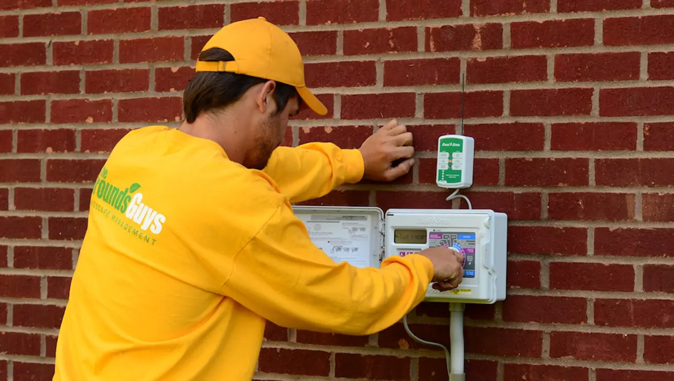 The Grounds Guys service professional adjusting a smart timer on the exterior of a home.