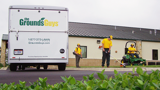 A team of The Grounds Guys service professionals cleaning up a business's lawn.