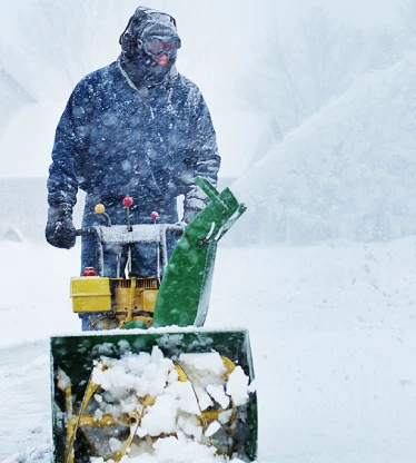 The Grounds Guys service professional using a snow blower during a snowstorm.