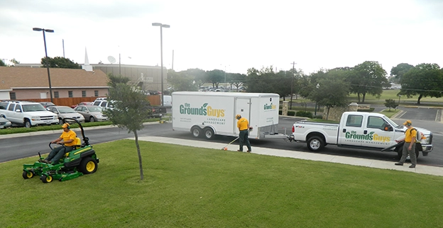 The Grounds Guys team mowing, edging, and cleaning up a commercial lawn.