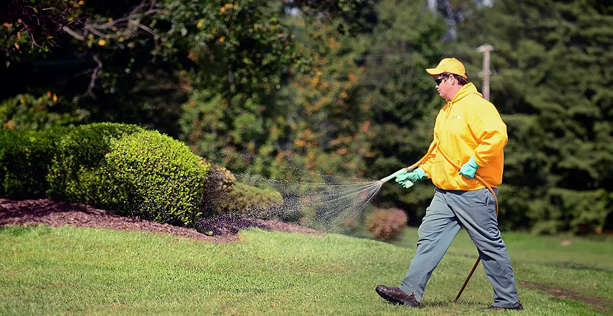 The Grounds Guys service professional spraying fertilizer on a lawn.