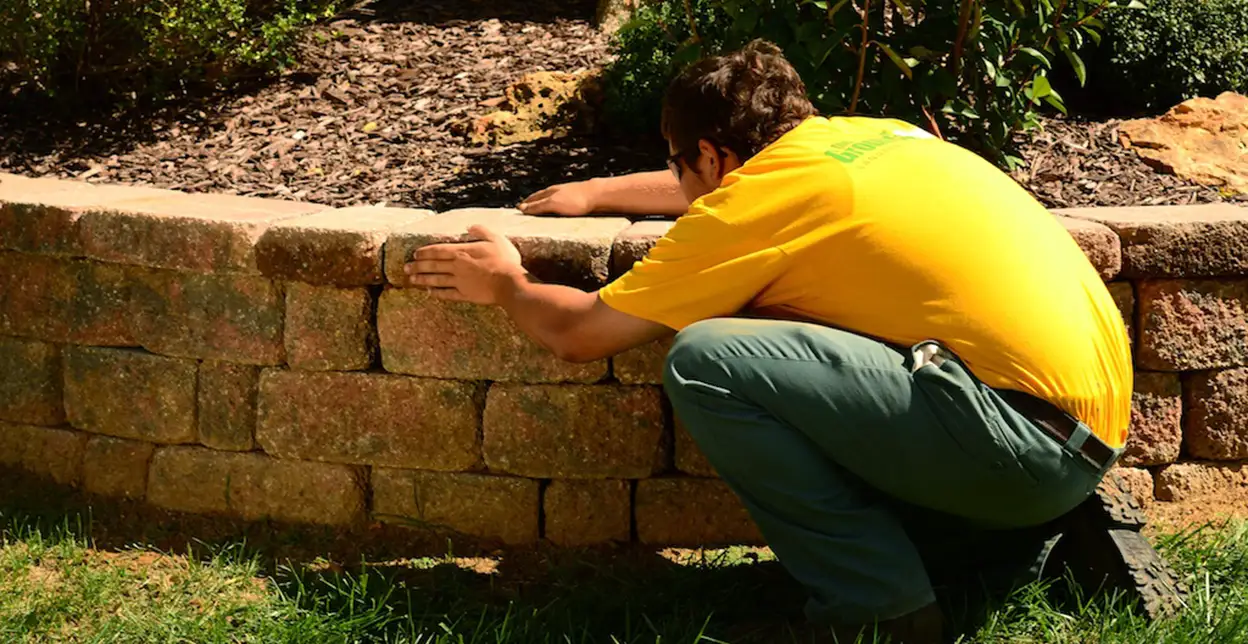 The Grounds Guys service professional adjusting a stone in the paver wall of a raised garden bed.