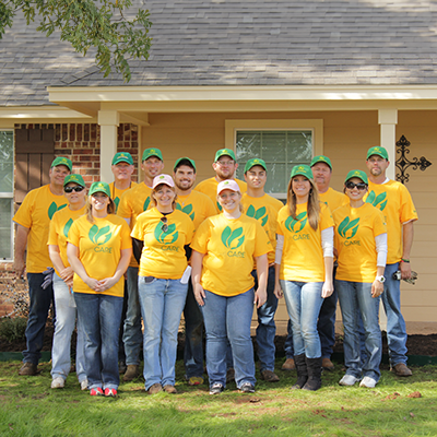 The Grounds Guys team wearing yellow branded shirts in front of a home.