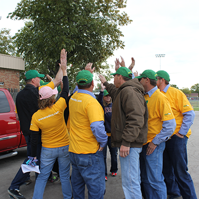 The Grounds Guys team wearing yellow branded shirts and high-fiving.