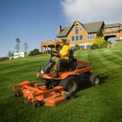 The Grounds Guys service professional mowing a large home's front lawn.