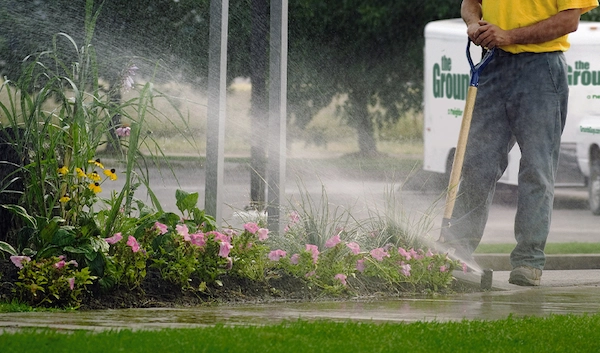 Sidewalk sprinkler beside an The Grounds Guys associate with branded van in background.