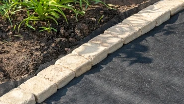 Landscape fabric on the ground next to a garden bordered by a row of white stones.